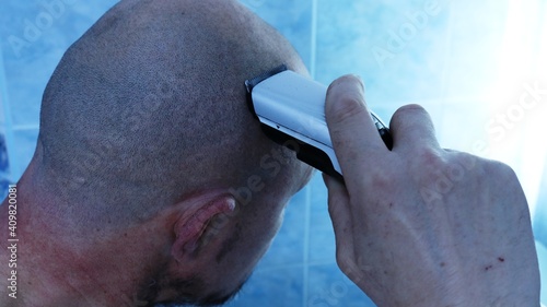 a man shaves his head baldly holding an electric hair trimmer in his hand in the neon lighting of a blue bathroom, the brutality and masculinity of the male image in the daily routine photo