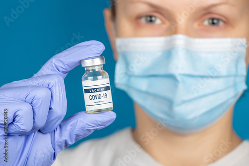 Vaccination coronavirus COVID-19. Coronavirus Vaccine in glass bottle in hand of doctor on blue background. Vaccine Concept of fight against coronavirus.