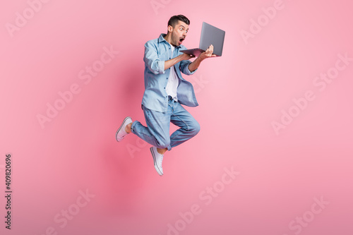 Full length body size photo of jumping programmer amazed working on laptop isolated on pastel pink color background