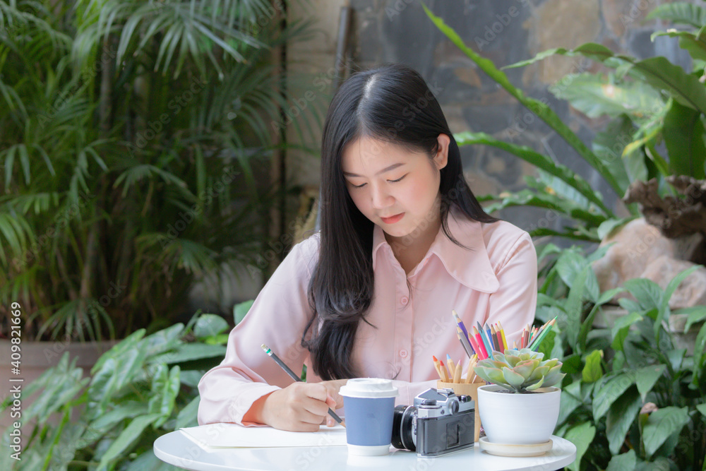 Young creative Asian woman sitting and using pencil to sketch or draw on paper. Young creative Asian woman sitting and using pencil to sketch or draw on paper.