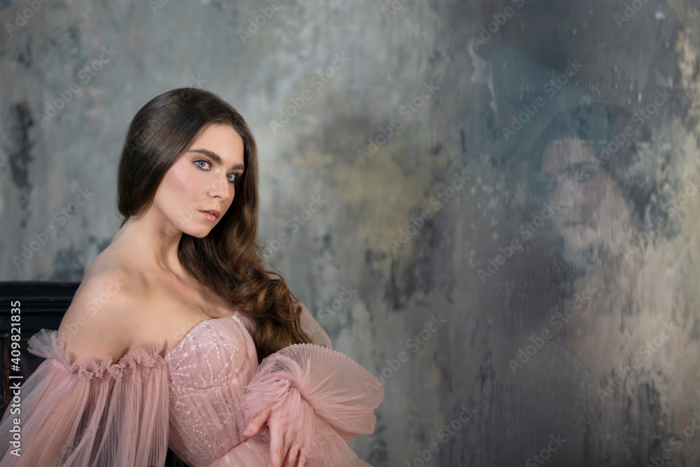 Delicate dark-haired woman in a light pink dress with delight on the wall Delicate dark-haired woman in a light pink dress with delight on the wall