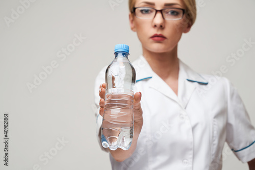 Portrait of young caucasian woman health care professional holding bottle of water standing over light grey background