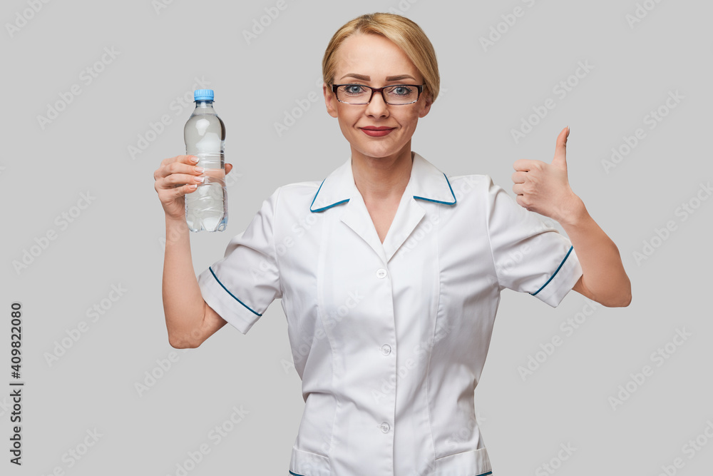 Portrait of young caucasian woman health care professional holding bottle of water standing over light grey background Portrait of young caucasian woman health care professional holding bottle of water standing over light grey background