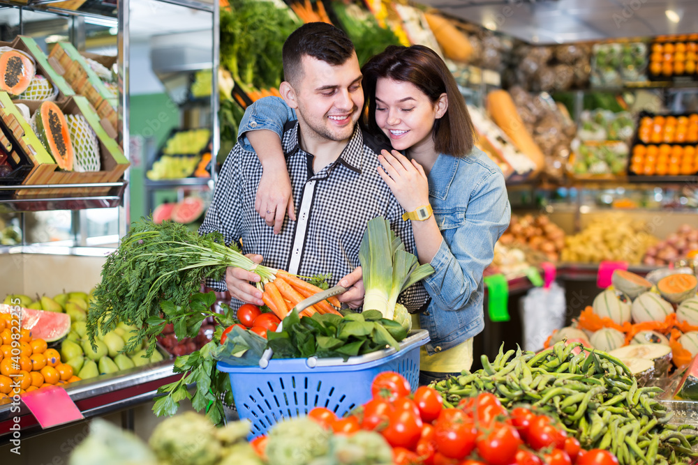Young cheerful couple choosing fresh vegetables in grocery shop