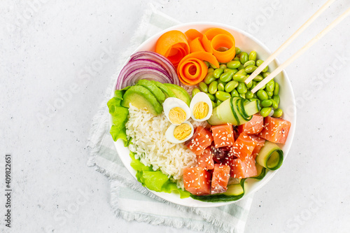 A portion of poke bowl with salmon fish, rice, avokado, red onion, cucumber, edamame beans, carrot and quail eggs, sesame seedes. White background.