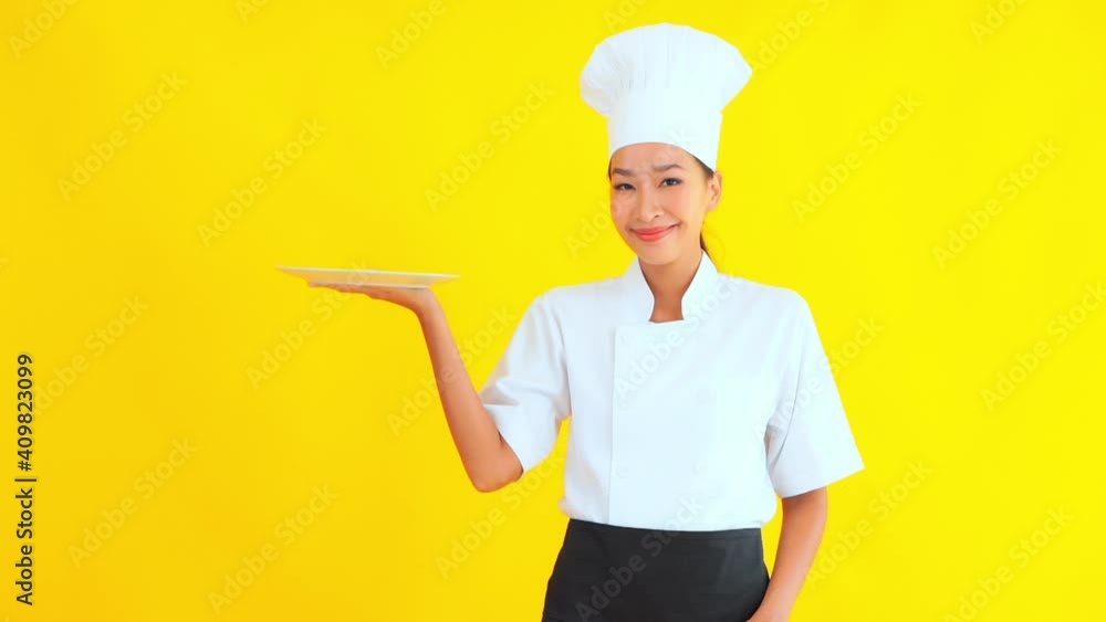 Asian woman with chef hat holding a plate thumbs up. Yellow screen in background Asian woman with chef hat holding a plate thumbs up. Yellow screen in background