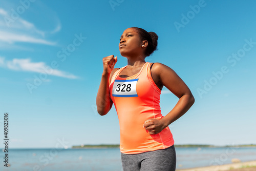 fitness, sport and race concept - young african american woman running marathon with badge number on shirt