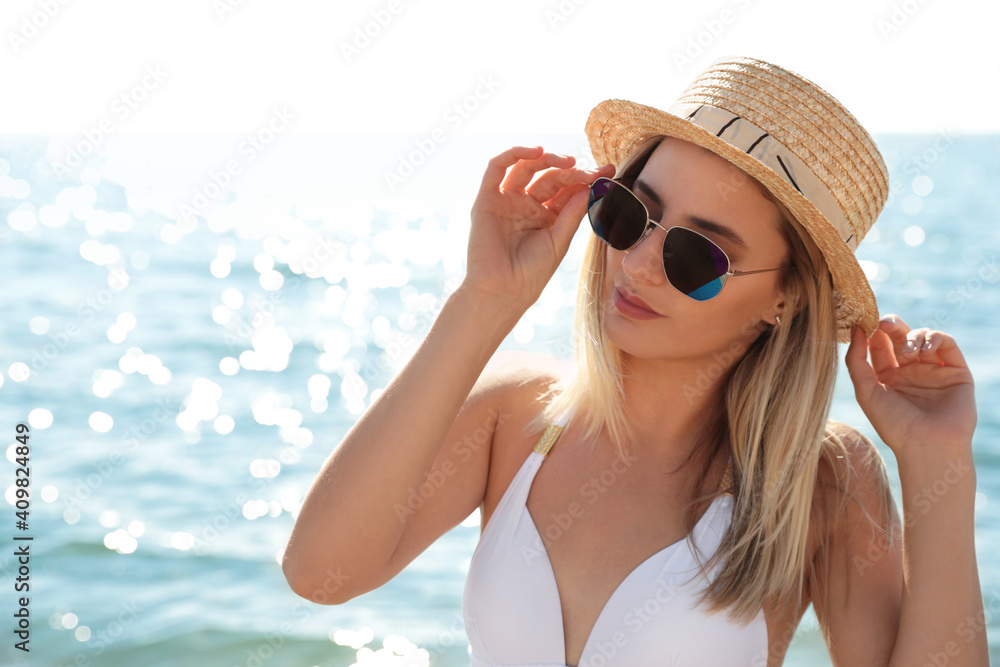Beautiful woman wearing sunglasses near sea on sunny day