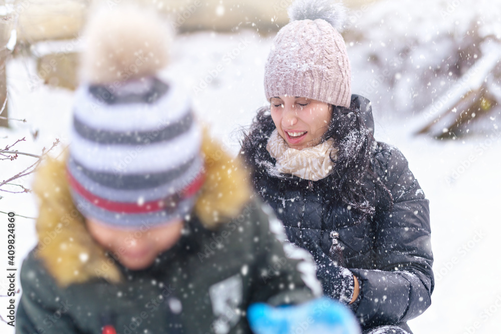 woman and son playing in winter outdoor, mother and child having fun on snowy winter, throwing snowballs woman and son playing in winter outdoor, mother and child having fun on snowy winter, throwing snowballs