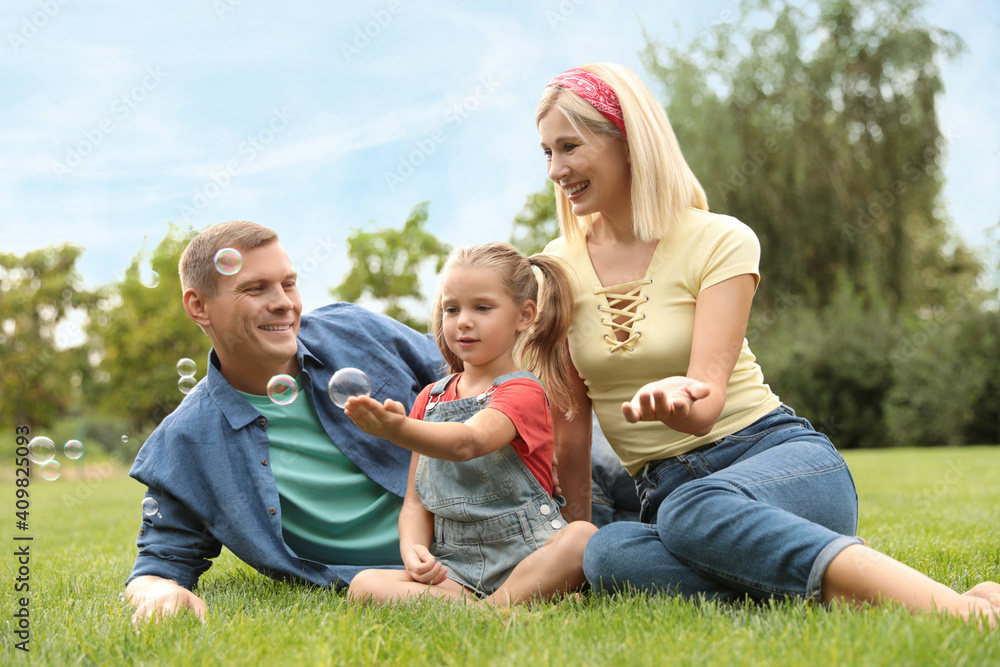 Happy family blowing soap bubbles in park on green grass Happy family blowing soap bubbles in park on green grass