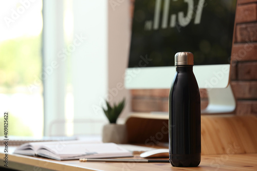 Modern black thermos bottle on wooden desk at workplace. Space for text photo
