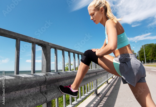 fitness, sport and healthy lifestyle concept - young woman stretching leg outdoors
