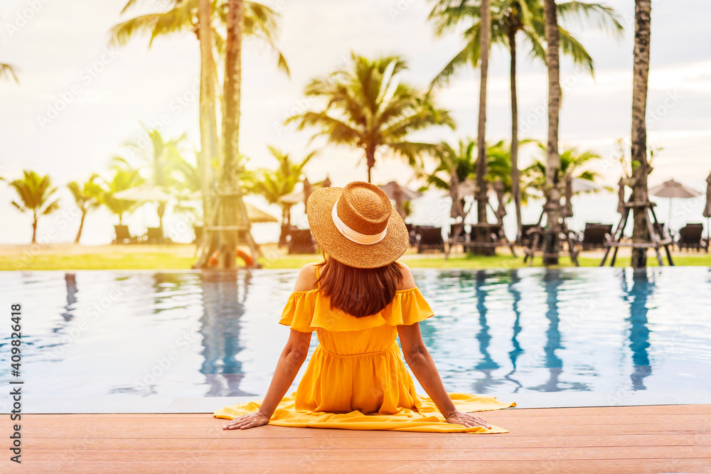 Young woman traveler relaxing and enjoying the sunset by a tropical resort pool while traveling for summer vacation - obrazy, fototapety, plakaty 