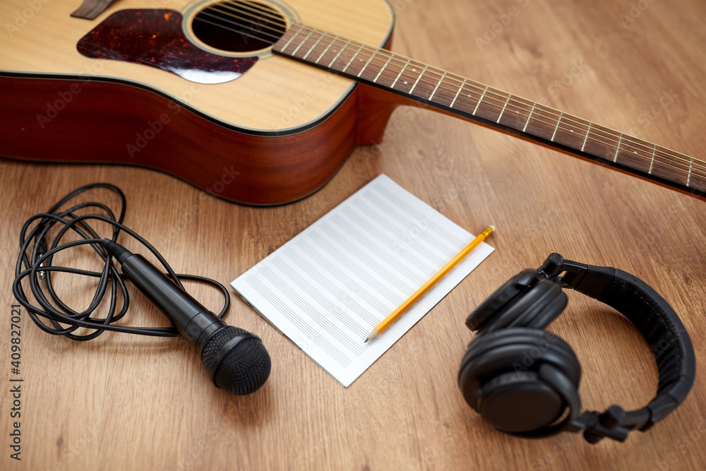 Naklejka premium composing and music writing concept - close up of acoustic guitar with music book, microphone and headphones on black table