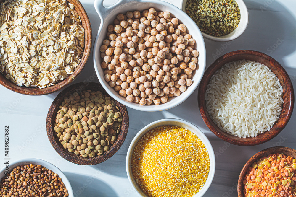 Flat lay of dry cereals, grains and legumes in white and wooden bowls, white background. Vegan protein concept. Flat lay of dry cereals, grains and legumes in white and wooden bowls, white background. Vegan protein concept.