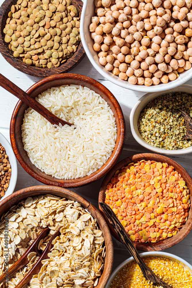Assorted dry cereals, grains and legumes in white and wooden bowls, white wooden background, top view. Vegan protein concept. Assorted dry cereals, grains and legumes in white and wooden bowls, white wooden background, top view. Vegan protein concept.