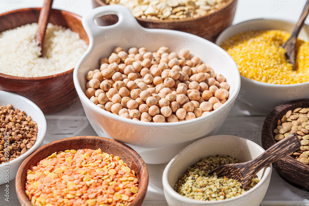 Raw chickpeas in a white bowl. Various dry cereals and legumes in white and wooden bowls, white wooden background. Vegan protein concept. Raw chickpeas in a white bowl. Various dry cereals and legumes in white and wooden bowls, white wooden background. Vegan protein concept.