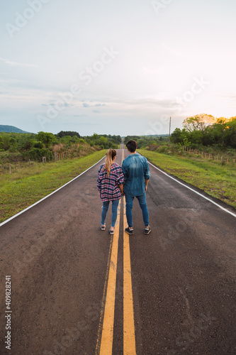 Young couple look at the horizon on the road.  Couple with their backs to each other on the road. © René Stevens