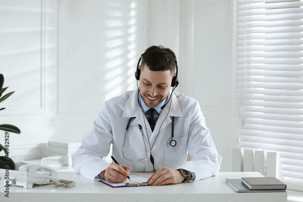 Doctor with headset consulting patient over phone at desk in clinic. Health service hotline