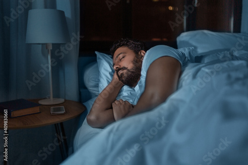 people, bedtime and rest concept - indian man sleeping in bed at home at night photo