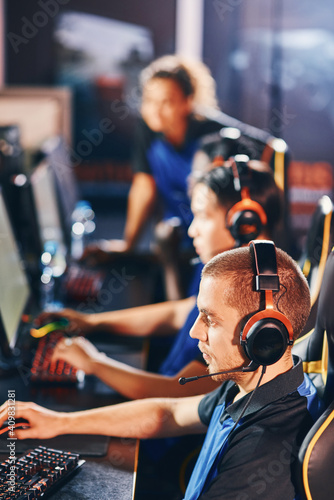 Vertical shot of professional cybersport gamers wearing headphones sitting in a row, playing online video games while participating in eSport tournament