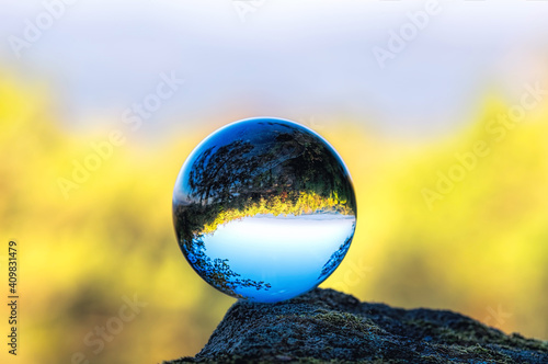 A glass ball standing on a rock reflects the autumn landscape and sky