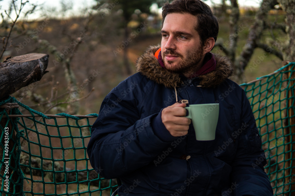 Photo of a young and attractive man having a coffee in the middle of a forest wearing winter clothes. Calm, empty place. Photo of a young and attractive man having a coffee in the middle of a forest wearing winter clothes. Calm, empty place.