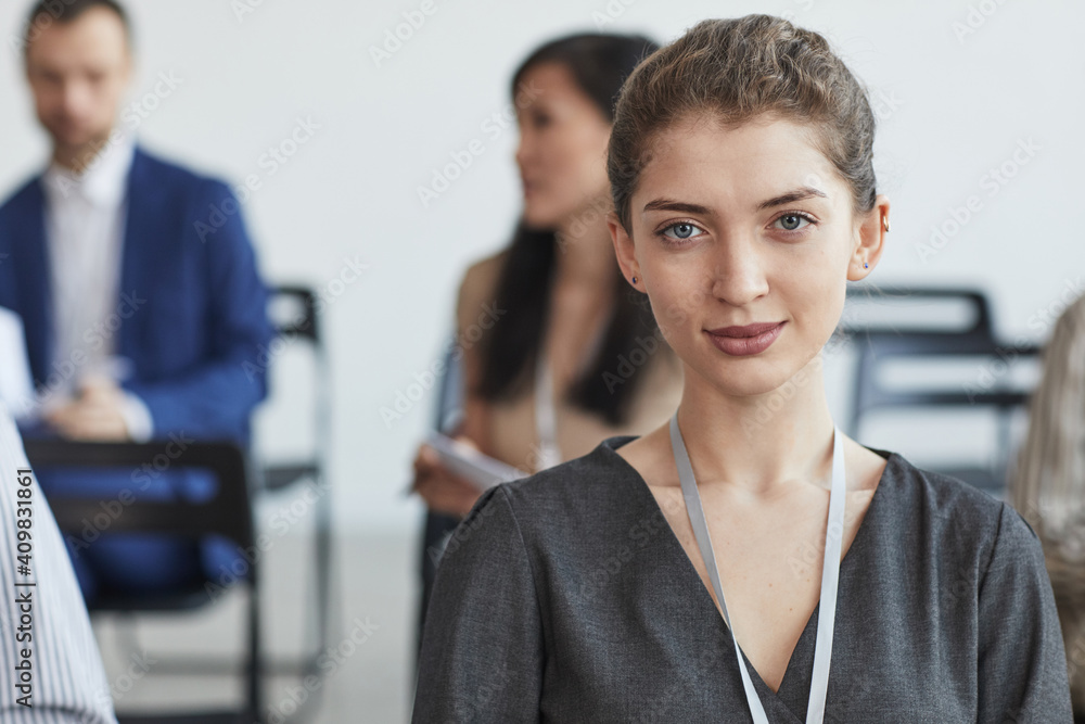 Head and shoulders portrait of young businesswoman looking at camera while sitting in audience at business conference or seminar, copy space Head and shoulders portrait of young businesswoman looking at camera while sitting in audience at business conference or seminar, copy space