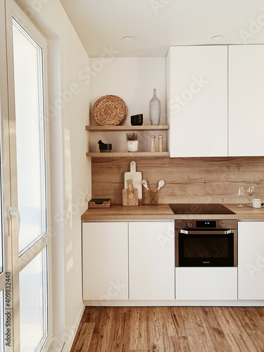 Stylish boho home kitchen interior concept. Wooden shelfs, dishes, utensils, vases, decorations. Cozy white comfortable interior design.