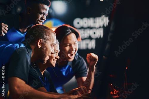Team of excited professional cybersport gamers looking at PC screen and celebrating success while participating in eSport tournament. Playing online video games © Friends Stock