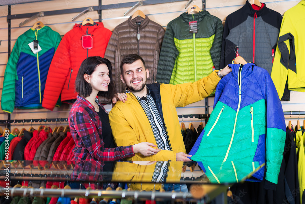 Positive couple examining windcheaters in sports clothes store