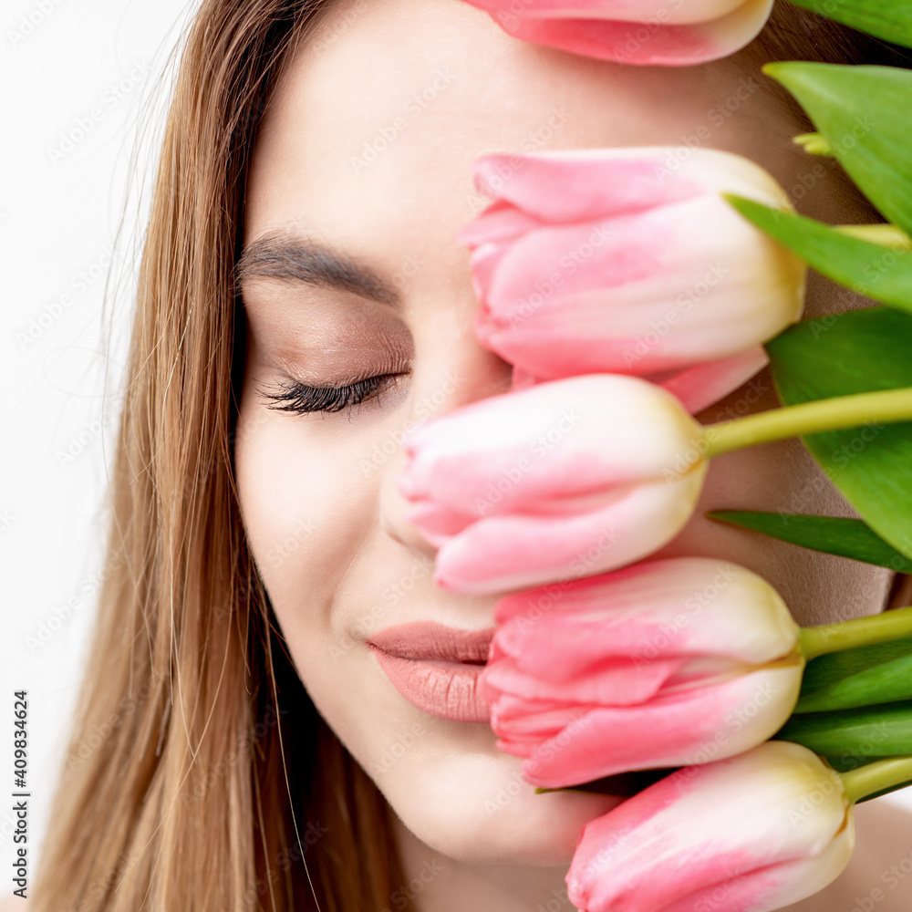 A portrait of a happy young caucasian woman with closed eyes and pink tulips cover her face against a white background A portrait of a happy young caucasian woman with closed eyes and pink tulips cover her face against a white background