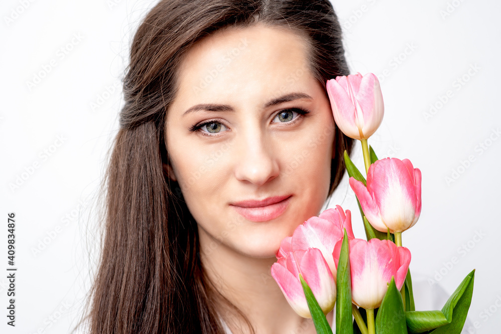 Portrait of a happy young caucasian woman with pink tulips against a white background