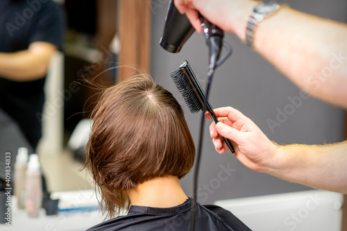 Hairdresser dries brown hair of the young woman in a beauty salon