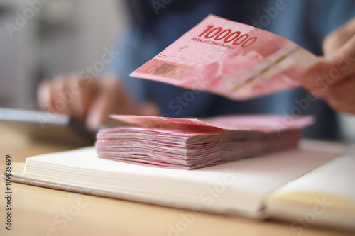 Close up of woman hand counting money uang Indonesian rupiah and making notes, money financial management photo