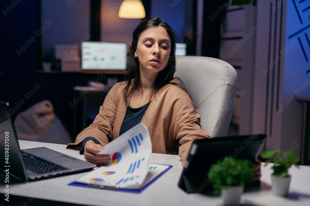 Entrepreneur reading income message from touchpad while trying to finish a deadline late at night. Business woman working overtime at the office to finish a corporate job using tablet pc.