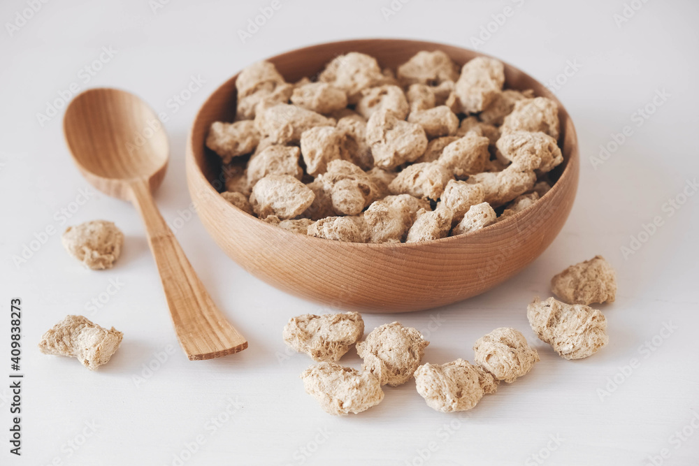 Raw dehydrated soy meat or dry soya chunks in wooden plate with a wooden spoon on white background. Top view. Copy, empty space for text Raw dehydrated soy meat or dry soya chunks in wooden plate with a wooden spoon on white background. Top view. Copy, empty space for text