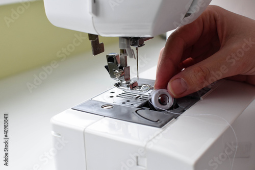 A woman's hand inserts a shuttle into a sewing machine