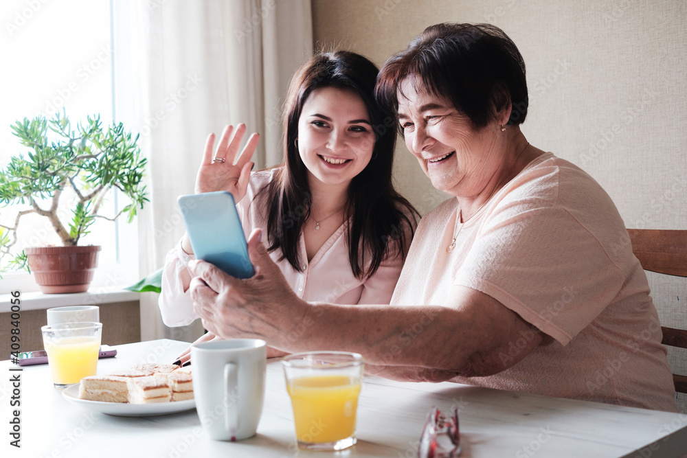 Grandmother and granddaughter communicate together with relatives via video communication - An elderly woman and her daughter communicate with friends via the Internet using the phone during COVID-19 Grandmother and granddaughter communicate together with relatives via video communication - An elderly woman and her daughter communicate with friends via the Internet using the phone during COVID-19