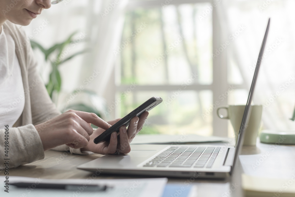 Woman sitting at desk and connecting with her smartphone Woman sitting at desk and connecting with her smartphone