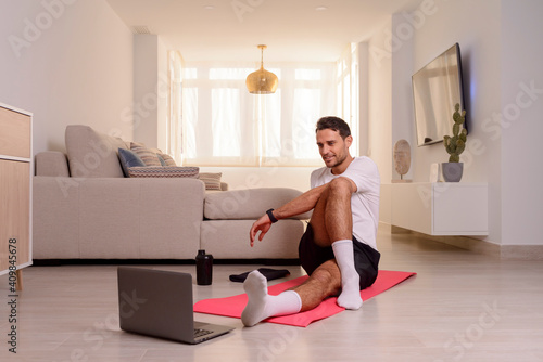 Young man smiling and stretching at home in front of a laptop..Online workout.