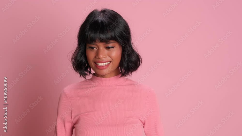Dark skinned brunette woman is sincerely happy that she finally got what she really wanted. Woman in casual clothes stands against background of pink wall and waves his hands with joy. Dark skinned brunette woman is sincerely happy that she finally got what she really wanted. Woman in casual clothes stands against background of pink wall and waves his hands with joy.