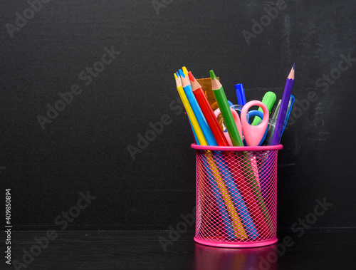 pink stationery glass with multi-colored wooden pencils and pens, black chalkboard background,