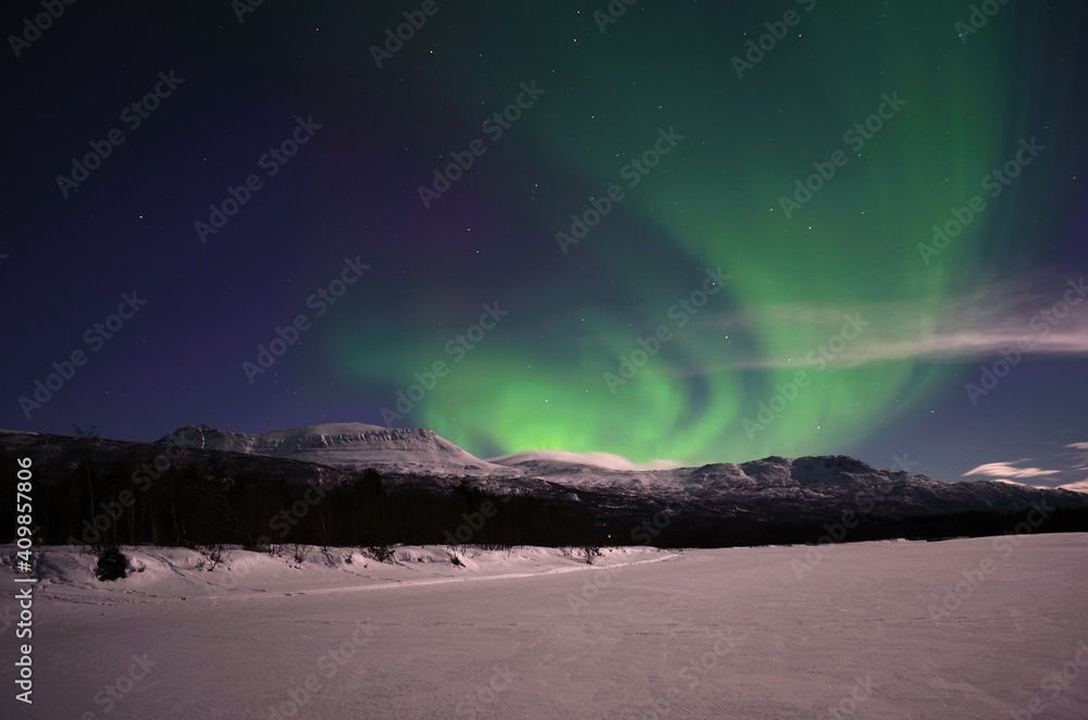 strong aurora borealis, northern light, over snowy mountain and moon lit landscape in the arctic circle night