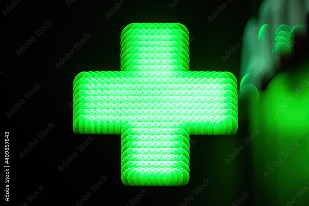 Obraz premium The defocused blurry view of pharmacy (drug store) green cross in the night. Artistic blur of vintage lens, abstract image.