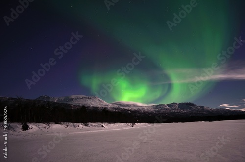 strong aurora borealis  northern light  over snowy mountain and moon lit landscape in the arctic circle night
