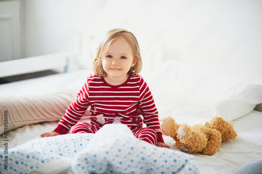 Happy toddler girl in striped red and white pajamas sitting on bed right after awaking Happy toddler girl in striped red and white pajamas sitting on bed right after awaking