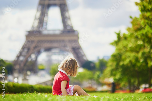Unhappy and gloomy toddler girl sitting on the grass near the Eiffel tower in Paris © Ekaterina Pokrovsky