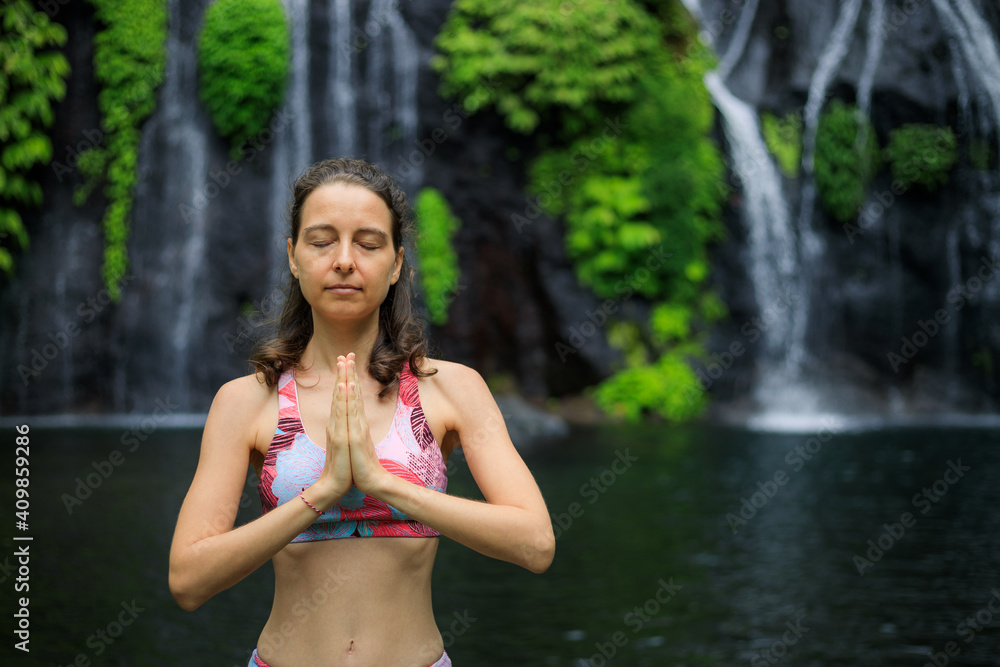 Obraz premium Close up of namaste mudra. Young woman meditating, practicing yoga and pranayama with namaste mudra near waterfall. Yoga outdoor concept. Copy space. Banyumala waterfall Wanagiri, Bali.