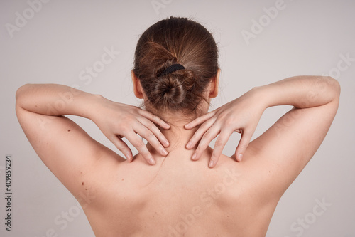 Young woman topless back view, arms to shoulders, isolate on gray background.